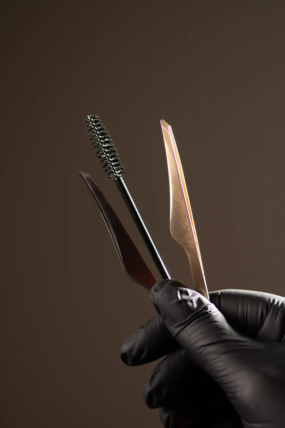 Pinsel und Pinzette zur Korrektur der Augenbrauenhaare in der Hand auf schwarzem Hintergrund